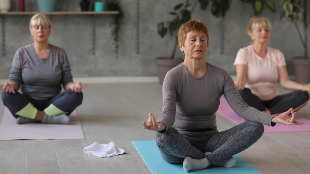 Three older women practice yoga on mats in a studio.