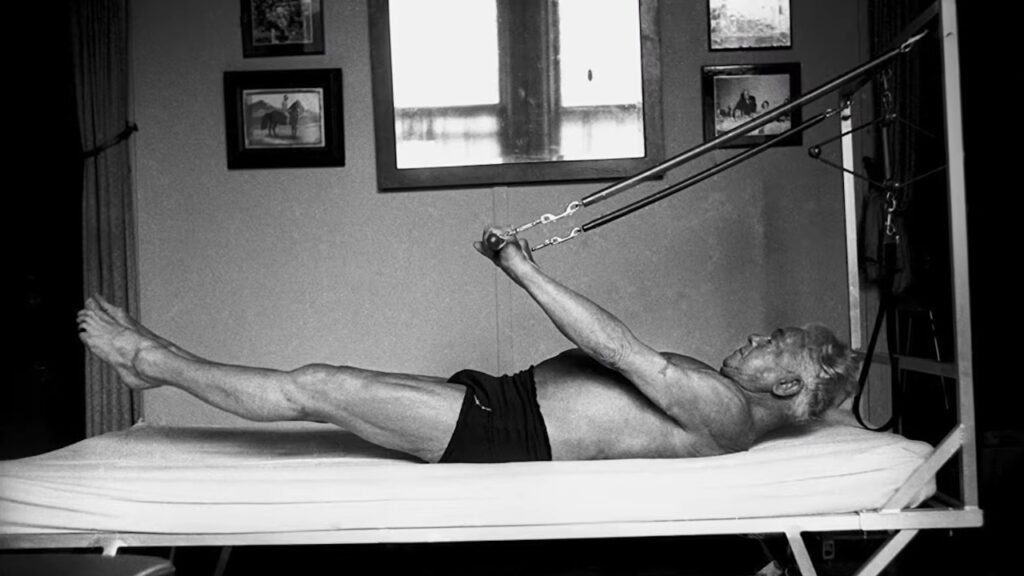 A man lies on a Pilates apparatus and exercises with resistance springs.