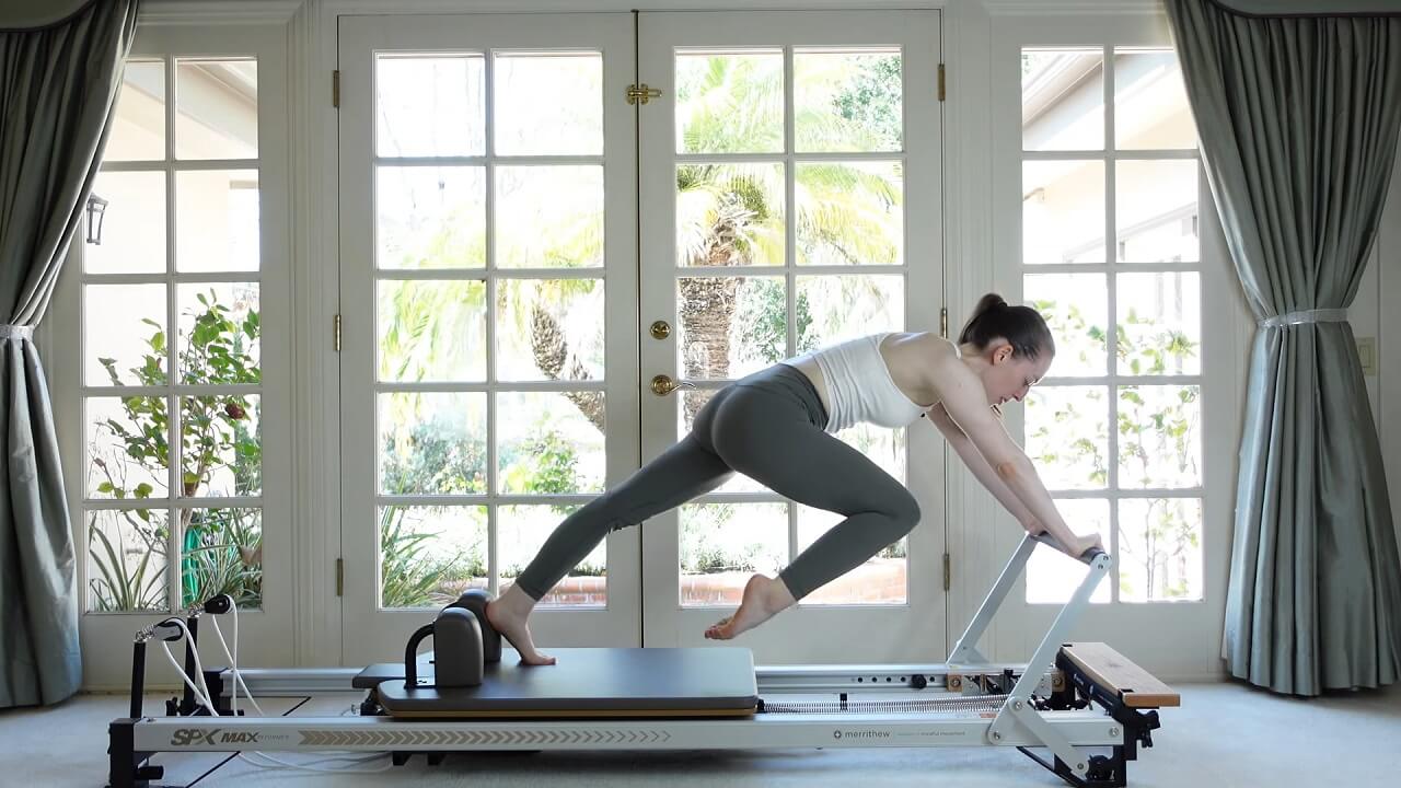 Woman exercising on a Pilates Reformer with her hands on the footbar and one foot on the carriage