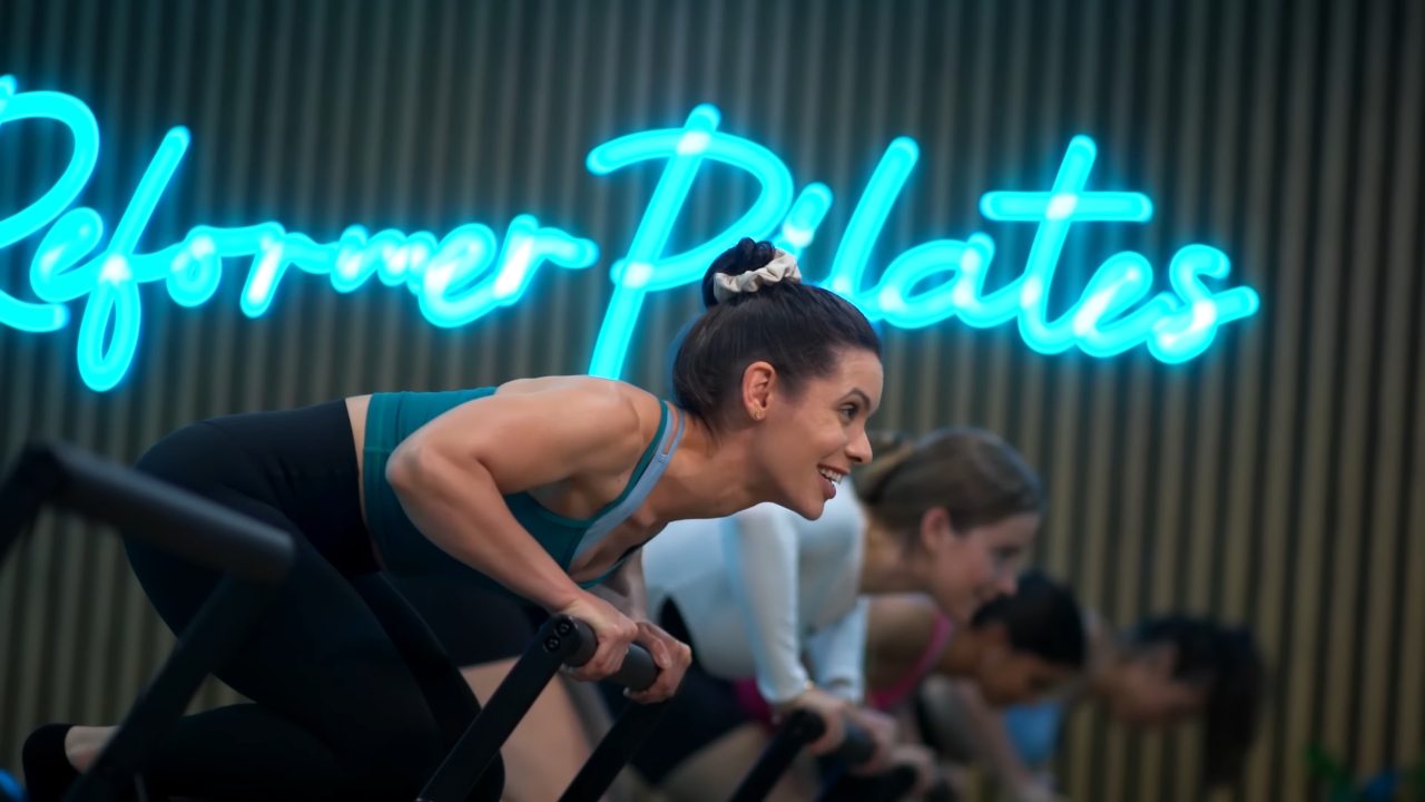 Woman practices Reformer Pilates during a group studio class.