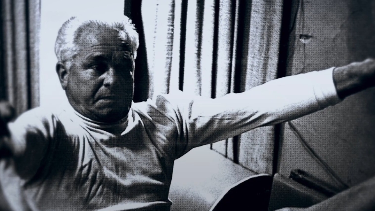 Joseph Pilates demonstrates an exercise with his arms extended.