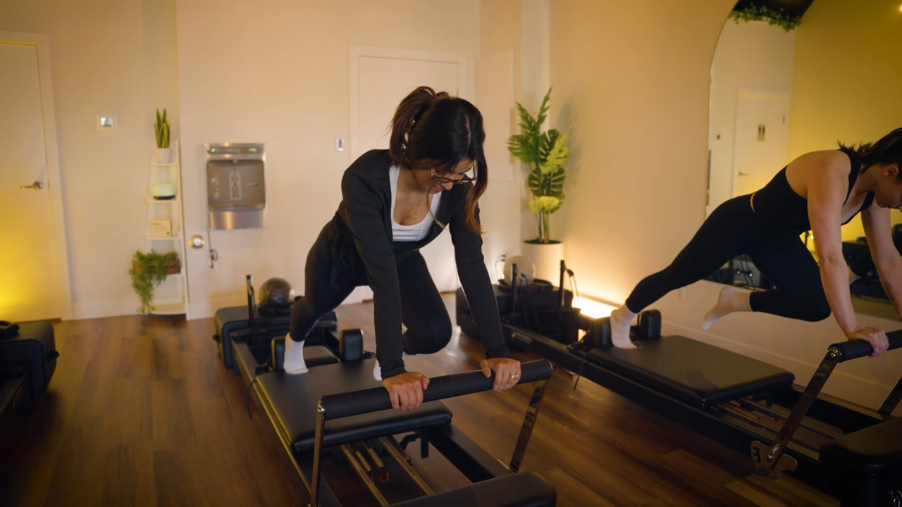 Two women exercise on Reformer Pilates machines in a studio.
